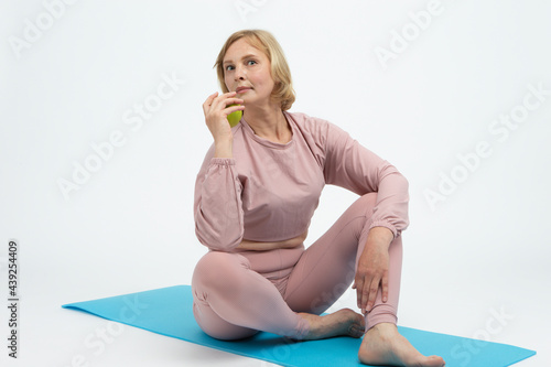 Natural Portrait of Mature Caucasian Woman Practicing Yoga In Sport Outfit With Green Apple Over White Background. photo