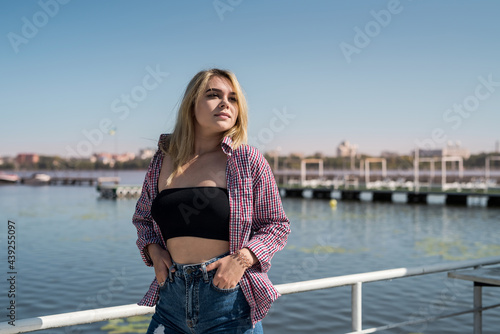 pretty young woman in casual wear standing in the city park near the pond summer day