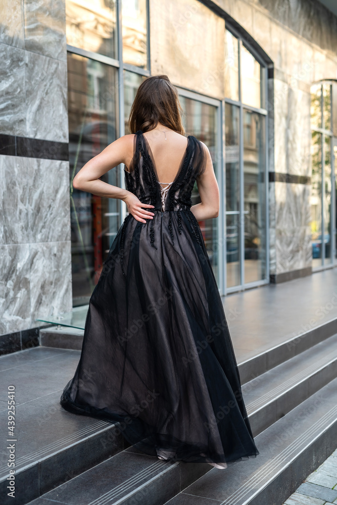 Fashion young woman full length in evening black dress walking in city daytime