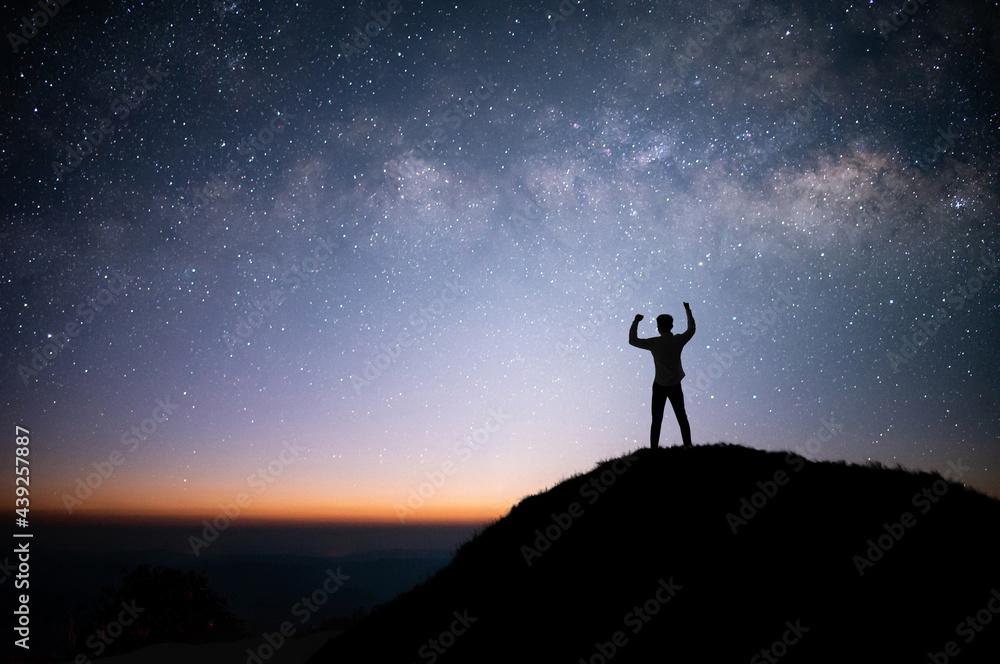 Silhouette of businessman standing on top of the mountain over the sky and star, milky way and Raise both hands to show happiness.