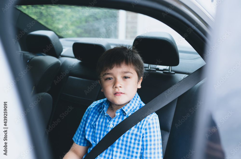 Cinematic portrait boy siting in safety car seat looking at camera with smiling face,Child sitting in the back passenger seat with a safety belt, School kid traveling to school by car.Back to school
