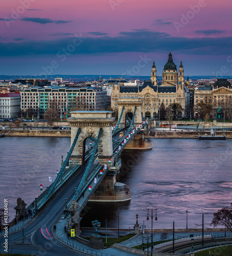 Budapest, Hungary - The famous Szechenyi Chain Bridge (Lanchid) at sunset decorated with national flags celebrating the 15th of March 1848 civic revolution day. St.Stephen's Basilica and magenta sky photo