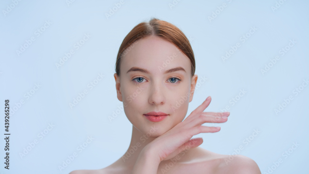Young attractive ginger woman posing for beauty products commercial. Touch her face, looks at camera and smiles Young attractive ginger woman posing for beauty products commercial. Touch her face, looks at camera and smiles