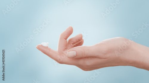 Female skin care model lifts her hand with a drop of cream on forefinger up and down twice against blue ripple background | Skin care cream commercial
