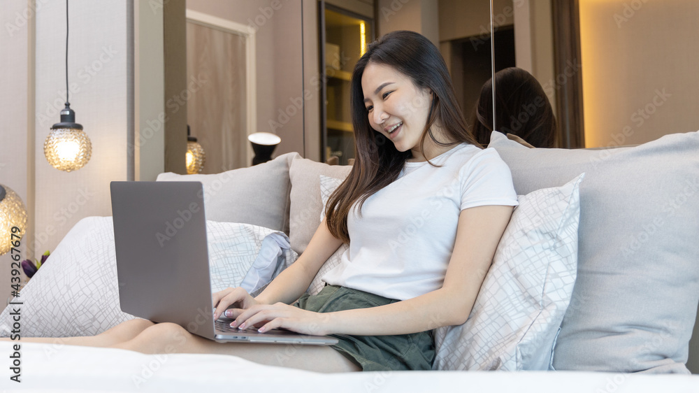 Asian woman uses laptop on bed in modern bedroom at home after she wakes up in the morning, Entertaining or relaxing using laptop technology, Wake-up activities, Happy lifestyle. Asian woman uses laptop on bed in modern bedroom at home after she wakes up in the morning, Entertaining or relaxing using laptop technology, Wake-up activities, Happy lifestyle.