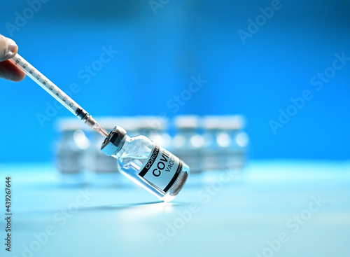 Doctor or Nurse hands holding the syringe with Coronavirus COVID-19 Vaccine Glass Bottle on blue surface with blue background at Thailand. Concept viruses spread throughout the world. Selective Focus.