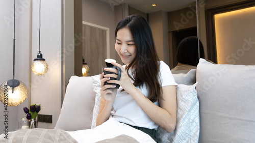 Asian woman sipping coffee on a luxurious bed in a manicured bedroom, After waking up have to drink coffee to refresh and get ready for a new day, relaxation, wake up morning, Hot coffee.