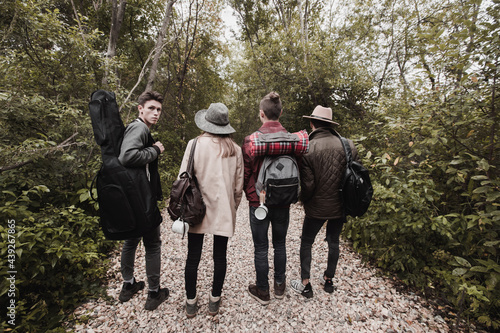 Back view of group of teenagers in warm clothes with guitar and backpacks standing in line on rocky road in forest © demphoto