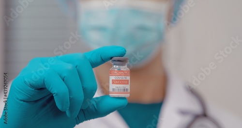 A male doctor with a stethoscope on shoulder holding syringe and COVID-19 vaccine. Healthcare And Medical concept. Coronavirus Vaccine concept in hand of doctor red vaccine jar.