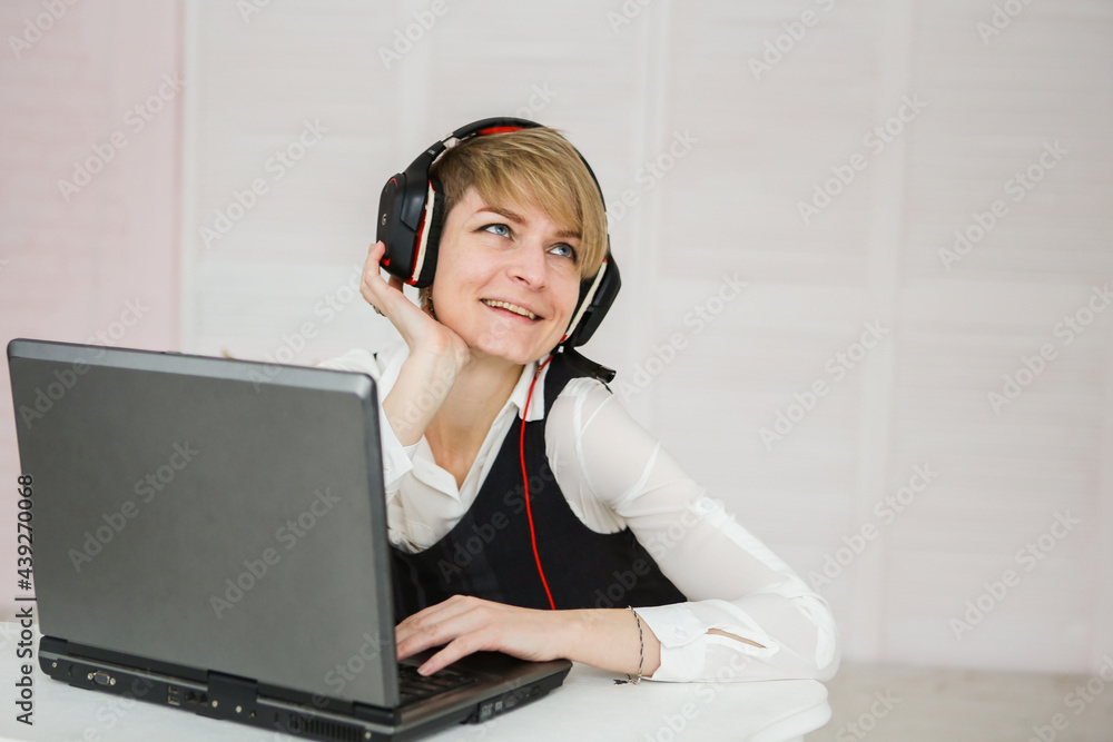 woman works at a laptop, wearing headphones and a microphone for communication woman works at a laptop, wearing headphones and a microphone for communication