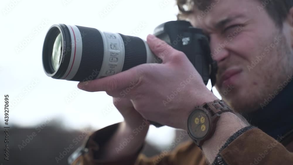 Man in a brown jacket puts a DSLR camera to his face,takes pictures. Man in a brown jacket puts a DSLR camera to his face,takes pictures.