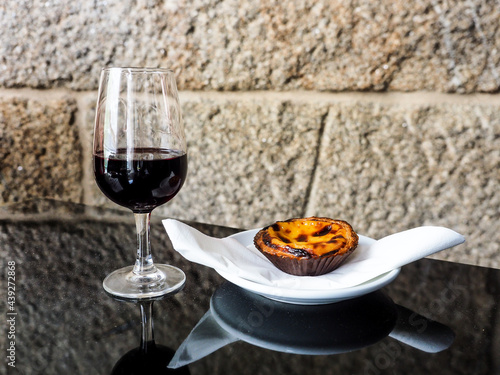 Una copa de vino de Oporto acompañada de un pastel de nata sobre un plato blanco, tipico de Portugal