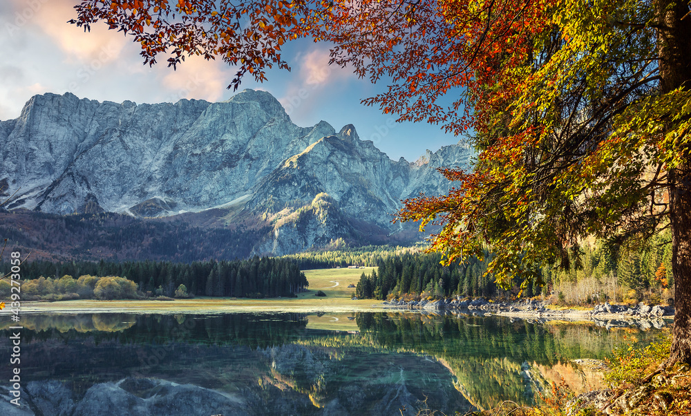Naklejka premium Autumn nature landscape of mountain valley. Amazing Fusine lake with Picturesque sky in sunny day. Picture of wild area. Popular locations for travel and hiking. Concept of resting on outdoor.