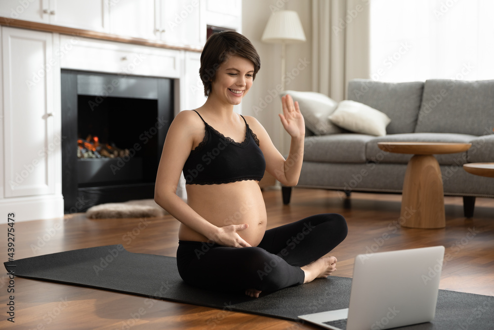 Smiling pregnant woman greeting trainer, preparing to online training, sitting on yoga mat, happy young future mom looking at laptop screen, involved in internet lesson, sport and pregnancy concept Smiling pregnant woman greeting trainer, preparing to online training, sitting on yoga mat, happy young future mom looking at laptop screen, involved in internet lesson, sport and pregnancy concept