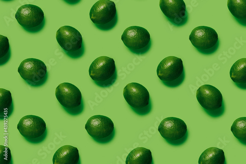 Geometrical pattern with limes isolated on a matching green background. Summer tropical fruit. Creative food concept. Flat lay, top view.