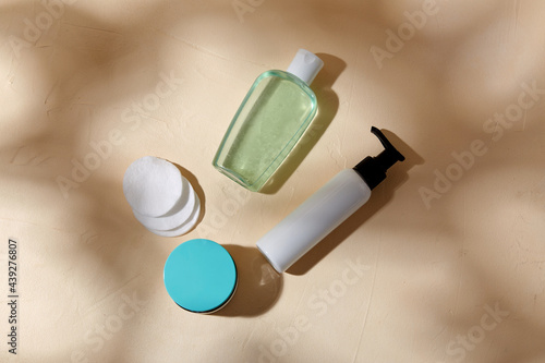 beauty, cosmetics and object concept - bottle of body milk, lotion, moisurizer and cotton pads on beige surface with shadows