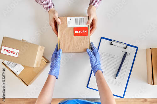 health protection, delivery and mail service concept - customer making return of parcel or purchase and worker in protective gloves receiving box photo