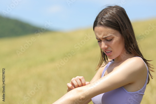 Allergic woman scratching itchy arm in a field
