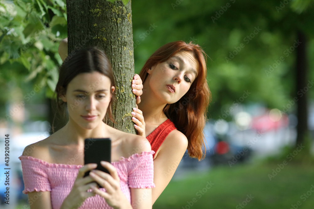 Woman using phone being spied by her friend Woman using phone being spied by her friend