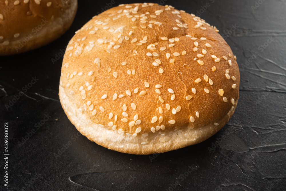 Sandwich bun with sesame seeds, on black stone background