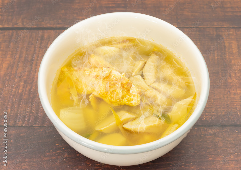 Hot soft tom yum soup with omelet, mushroom, galangal, lemongrass in white bowl on wood table Hot soft tom yum soup with omelet, mushroom, galangal, lemongrass in white bowl on wood table