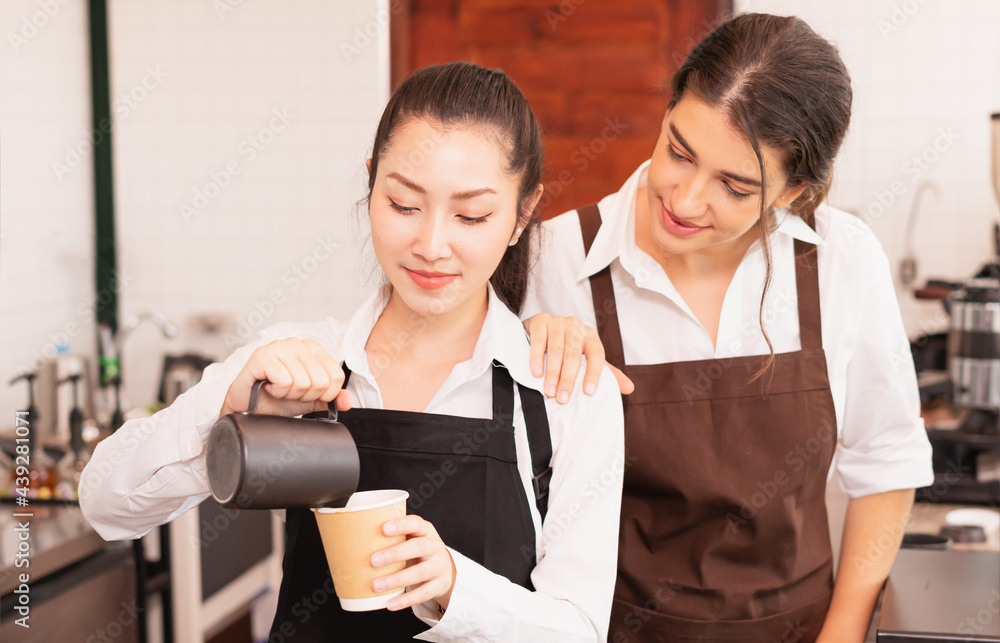 Focusing on half-body angle of Asian barista women fill milk into hot coffee cup, caucasian barista woman cheering to prepare coffee in cafe bar Focusing on half-body angle of Asian barista women fill milk into hot coffee cup, caucasian barista woman cheering to prepare coffee in cafe bar