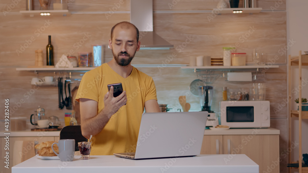 Man working from house with automation lighting system, sitting in kitchen switch off the lights using voice command to smart home application on smartphone. Person controlling light with wifi gadget Man working from house with automation lighting system, sitting in kitchen switch off the lights using voice command to smart home application on smartphone. Person controlling light with wifi gadget