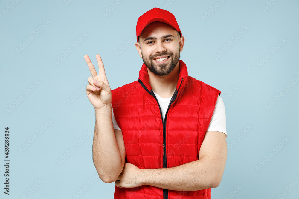 Professional delivery guy employee man in red cap white T-shirt vest uniform workwear work as dealer courier show v-sign isolated on pastel blue color background studio portrait Service concept Professional delivery guy employee man in red cap white T-shirt vest uniform workwear work as dealer courier show v-sign isolated on pastel blue color background studio portrait Service concept