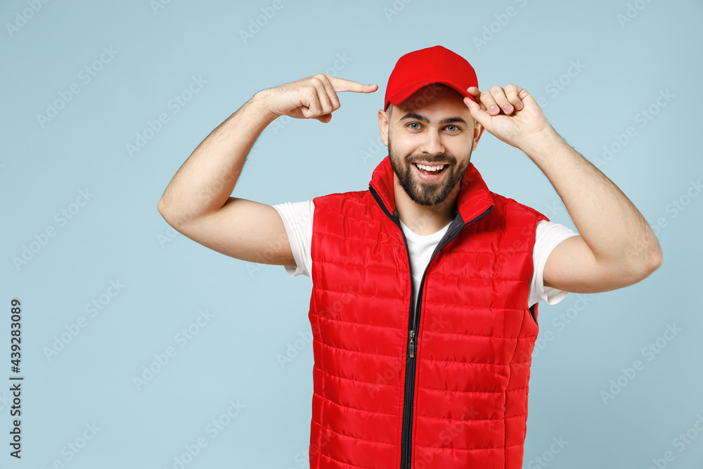 Professional delivery guy employee man in white T-shirt vest uniform workwear work dealer courier pointing finger on red cap isolated on pastel blue color background studio portrait. Service concept.