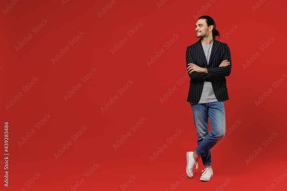 Full length fun young smiling happy businessman latin man 20s with long hair wearing black striped jacket grey shirt look aside hold hands crossed folded isolated on red background studio portrait Full length fun young smiling happy businessman latin man 20s with long hair wearing black striped jacket grey shirt look aside hold hands crossed folded isolated on red background studio portrait