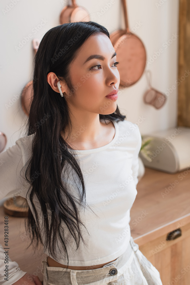 portrait of serious young asian woman in white blouse standing with earphones in kitchen portrait of serious young asian woman in white blouse standing with earphones in kitchen