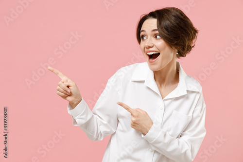 Young surprised employee business woman corporate lawyer in classic formal white shirt work in office point index finger aside on workspace area mock up copy space isolated on pastel pink background.