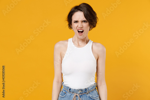 Young angry stressed annoyed indignant nervous woman 20s with bob haircut wearing white tank top shirt scream shout look camera isolated on yellow color background studio People lifestyle concept. © ViDi Studio