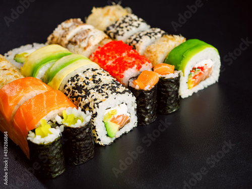 Sushi set, top view. Various sushi roll with salmon, avocado, cream cheese philadelphia and tobiko flying fish caviar on black background with red chopsticks