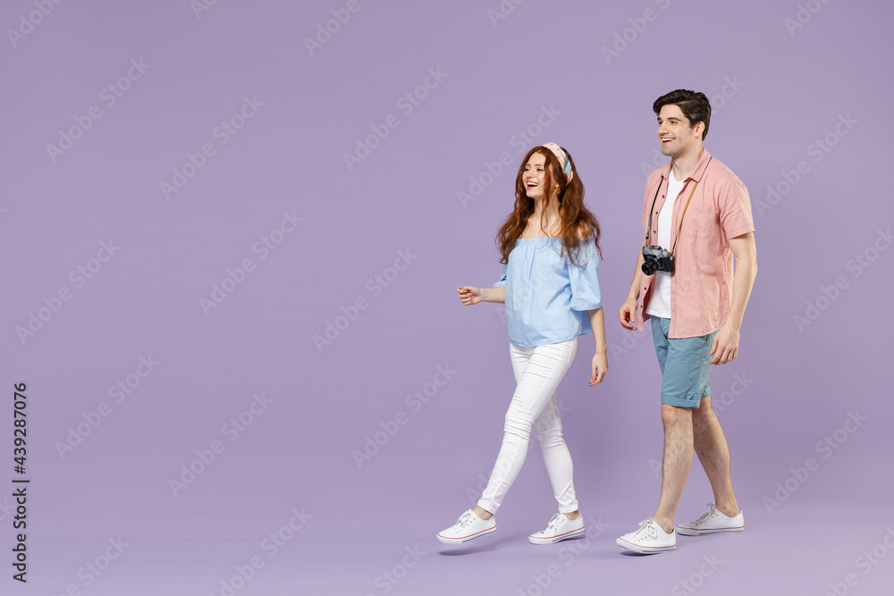 Naklejka premium Full length side view two happy traveler tourist woman man 20s couple in summer clothes wlak go isolated on purple background. Passenger travel abroad on weekends getaway. Air flight journey concept.