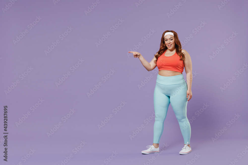 Full length young chubby overweight plus size big fat fit woman in red top warm up training point index finger aside copy space area isolated on purple background gym Workout sport motivation concept Full length young chubby overweight plus size big fat fit woman in red top warm up training point index finger aside copy space area isolated on purple background gym Workout sport motivation concept
