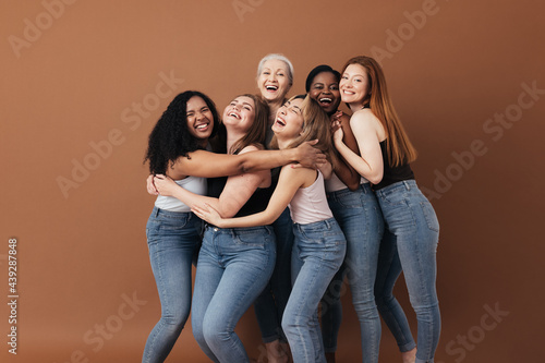 Six laughing women of a different race, age, and figure type. Group of multiracial females having fun against a brown background.