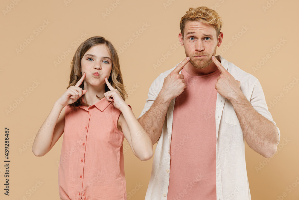 Young parent man have fun with child teen girl in casual clothes. Daddy look at little kid daughter pointing index fingers on blowing puffing cheeks with funny face mouth isolated on beige background - obrazy, fototapety, plakaty 