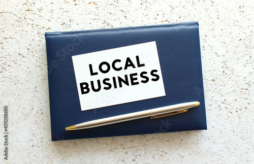 Text LOCAL BUSINESS on a business card lying on a blue notebook next to the pen. © Ihar