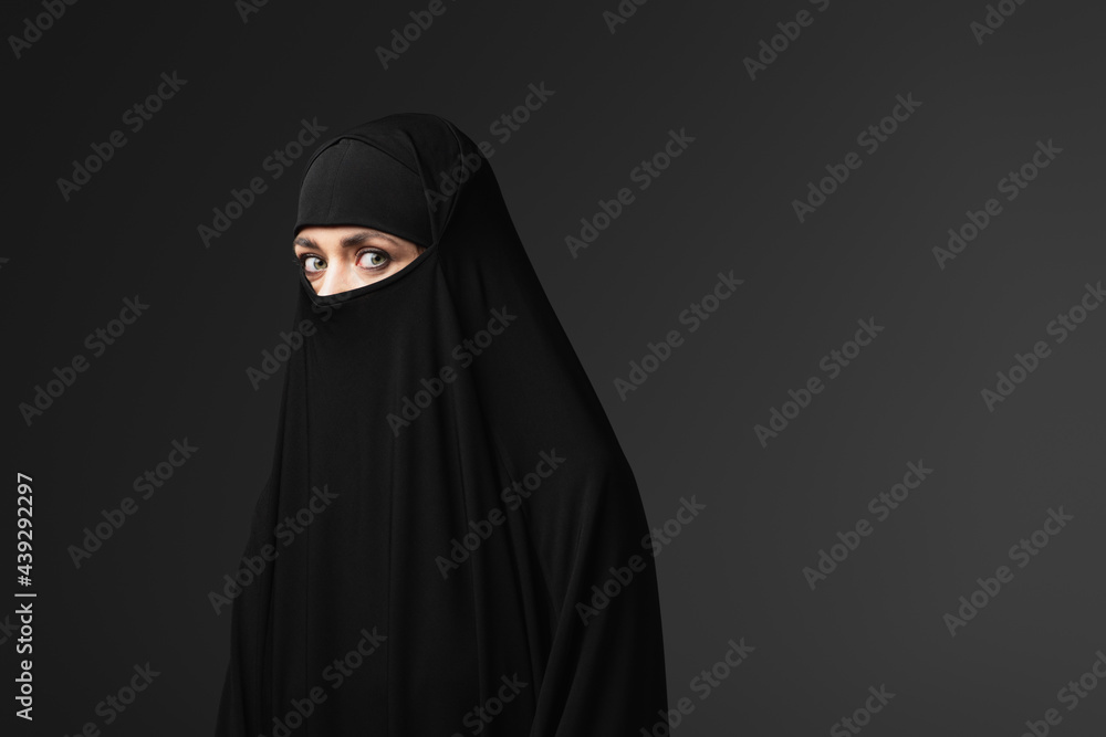 young muslim woman in black traditional clothing looking at camera isolated on black young muslim woman in black traditional clothing looking at camera isolated on black