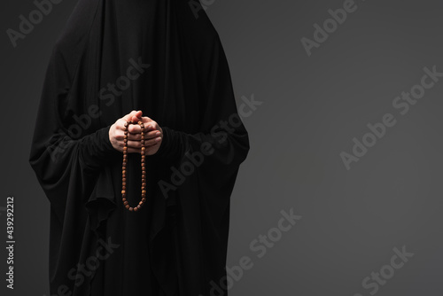partial view of muslim nun in black abaya holding praying beads isolated on dark grey photo