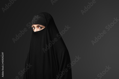young muslim woman in black traditional clothing looking at camera isolated on black