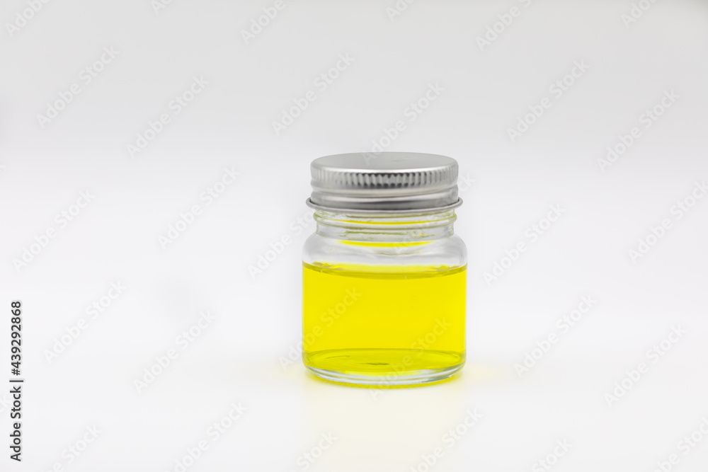Glass jar containing with silver lid and  yellow oil  display on white background.