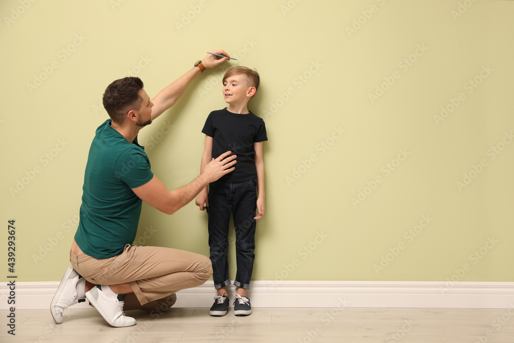 Father measuring height of his son near light wall indoors. Space for text Father measuring height of his son near light wall indoors. Space for text