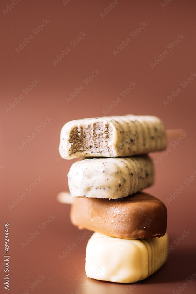 Different chocolate Popsicles lying on top of each other. brown background. top popsicle bitten Different chocolate Popsicles lying on top of each other. brown background. top popsicle bitten