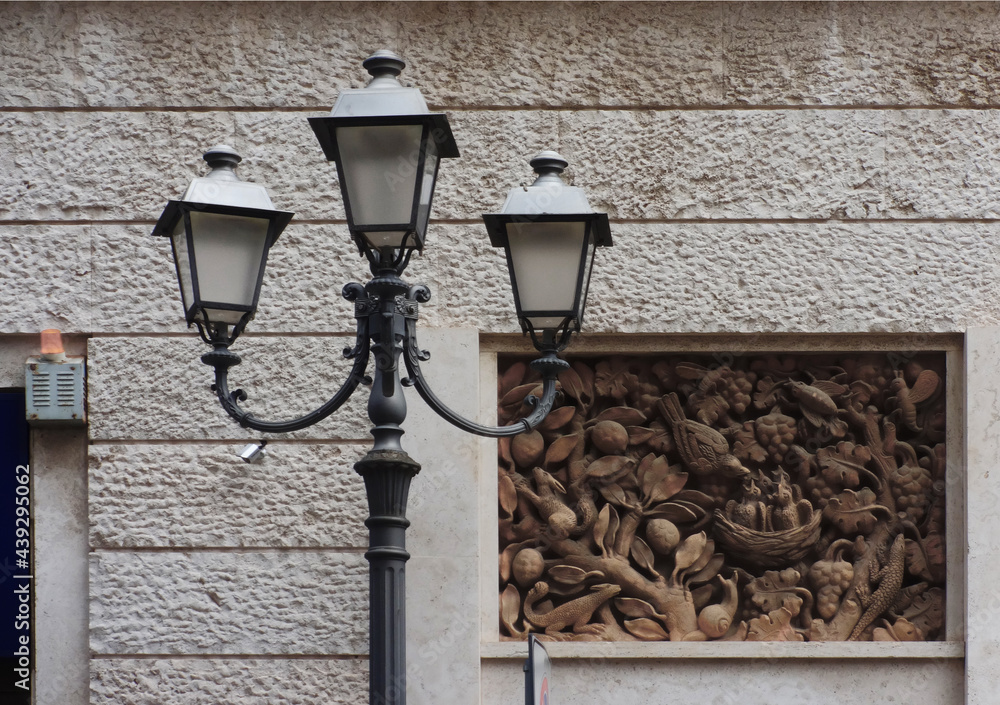 a street lantern against the backdrop of a stone wall and a relief work of art, Bridisi, Italy a street lantern against the backdrop of a stone wall and a relief work of art, Bridisi, Italy