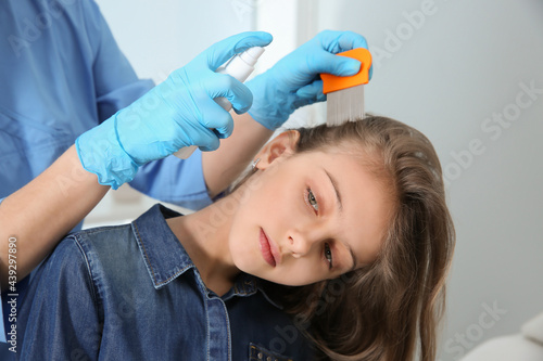 Doctor using nit comb and spray on girl's hair indoors. Anti lice treatment