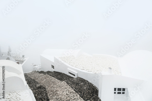 White architecture on Santorini island, Greece. Misty morning with heavy fog. White roofs of the houses and stairs down to the sea