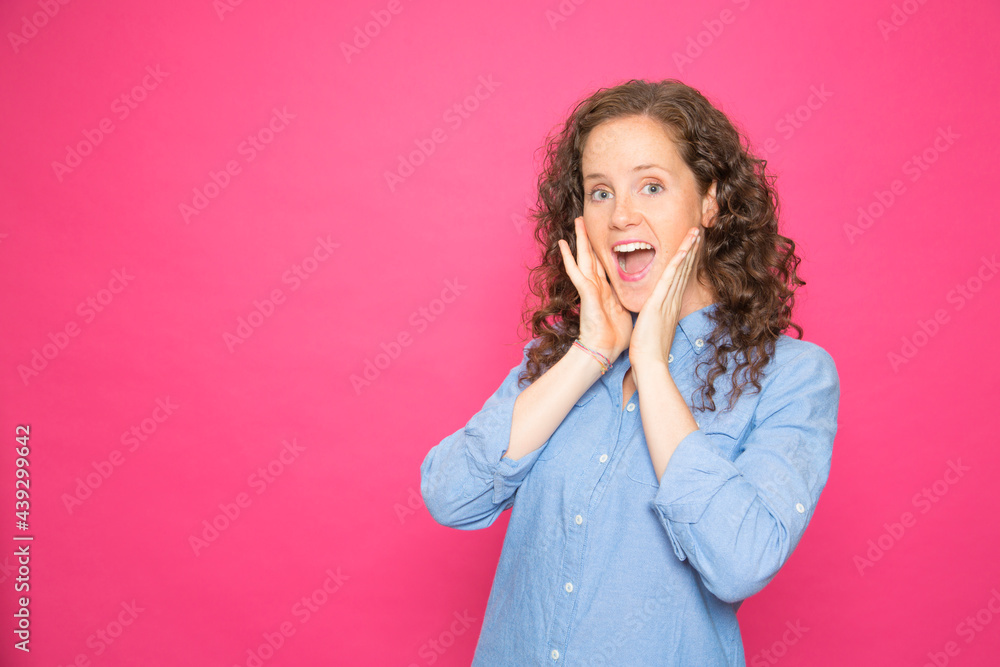 Portrait surprised young girl with hands on face looking at camera over pink background Portrait surprised young girl with hands on face looking at camera over pink background