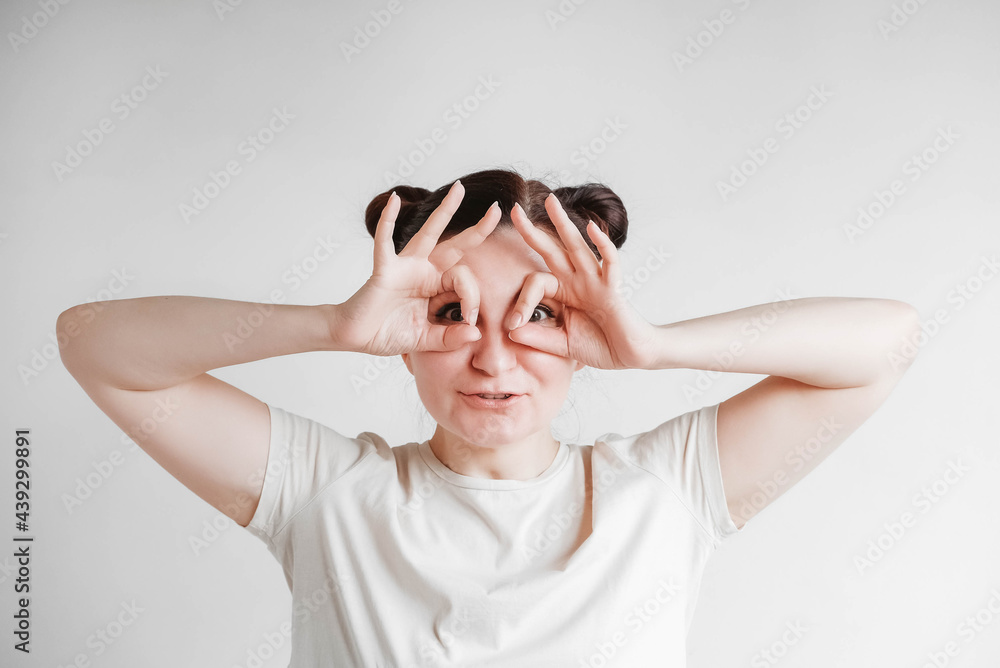 Portrait of a beautiful woman with her hands emitting glasses and a funny face wearing a T-shirt on a white background. Copy, empty space Portrait of a beautiful woman with her hands emitting glasses and a funny face wearing a T-shirt on a white background. Copy, empty space